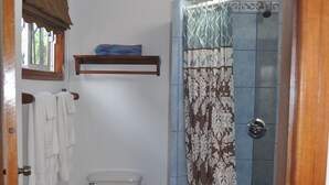 A bathroom with a toilet, a shower with a patterned curtain, a ceiling fan, and a window with a blind. - Latitude 17 Garden Room, heart of Hopkins Village, Belize (Hopkins Village)
