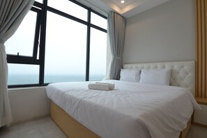 A bedroom with a large window, a bed with white bedding, and a view of the sea. - The Crystal Apartment (Bac Nha Trang)