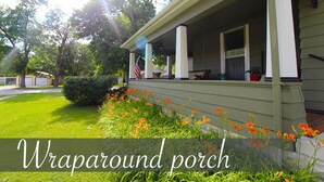 A wraparound porch with a green exterior, a flag, and orange flowers in the foreground. - Tastefully restored historic home in quaint town, 20 minute drive to Columbia MO (Centralia)