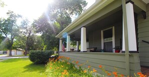 A wraparound porch with a green exterior, a flag, and orange flowers in the foreground. - Tastefully restored historic home in quaint town, 20 minute drive to Columbia MO (Centralia)
