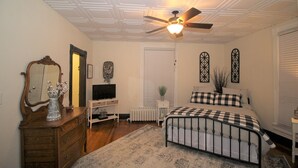 A bedroom with a bed, dresser, ceiling fan, and a window with decorative shutters. - Tastefully restored historic home in quaint town, 20 minute drive to Columbia MO (Centralia)