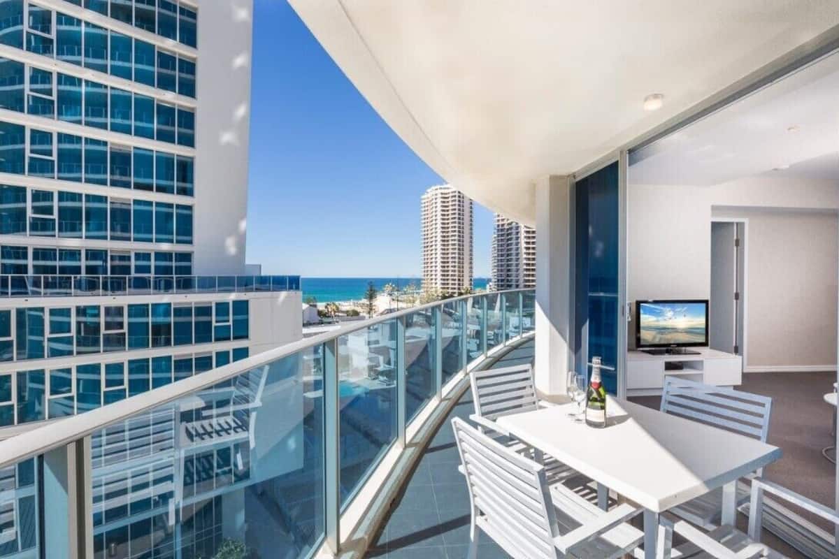 Un balcón con barandilla de cristal que da a una playa y edificios altos.
