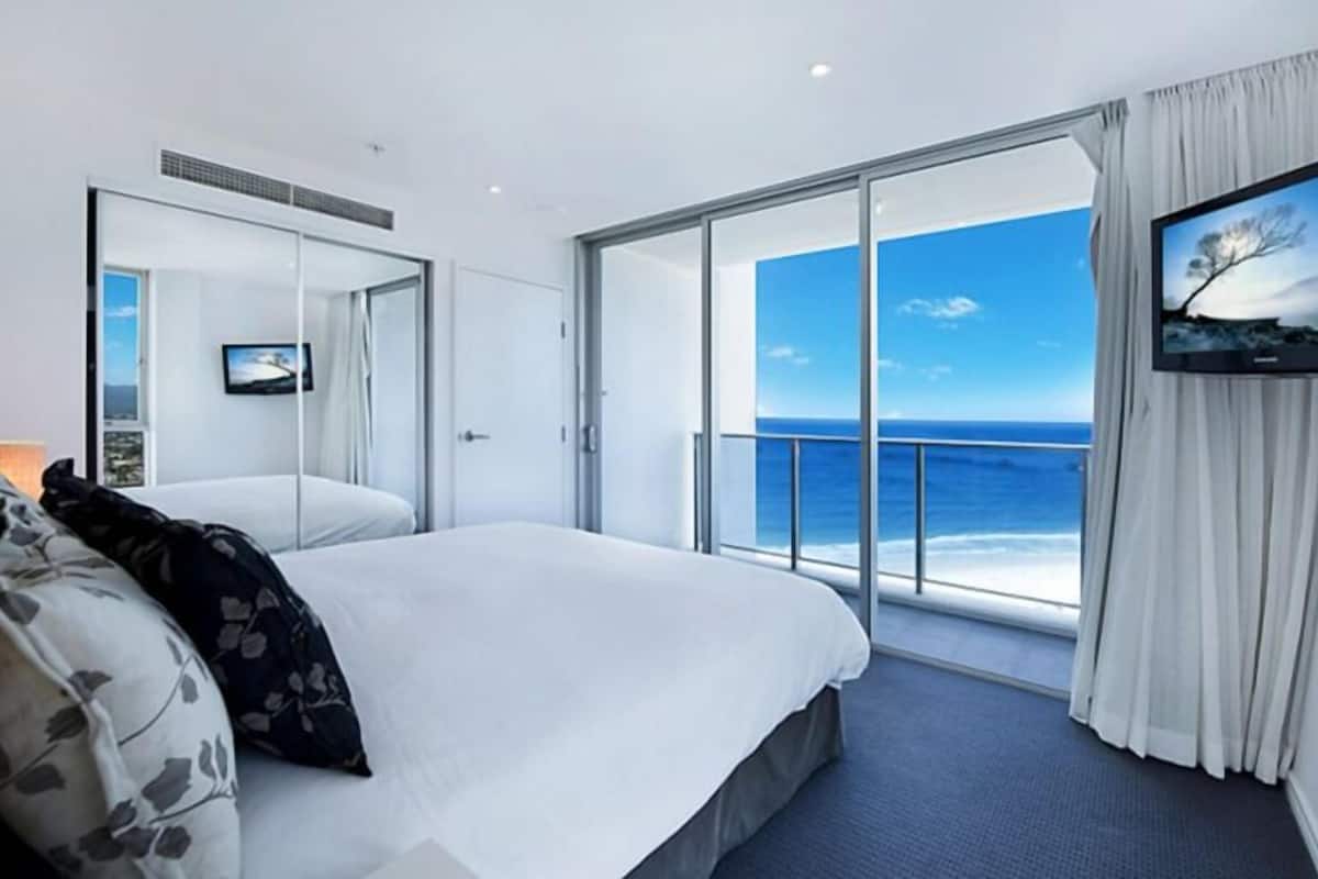 Una habitación de hotel moderna con una cama grande, televisión y un balcón con vista al océano.
