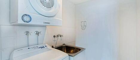 Un baño pequeño con lavamanos blanco, lavadora integrada y extractor de aire de pared.