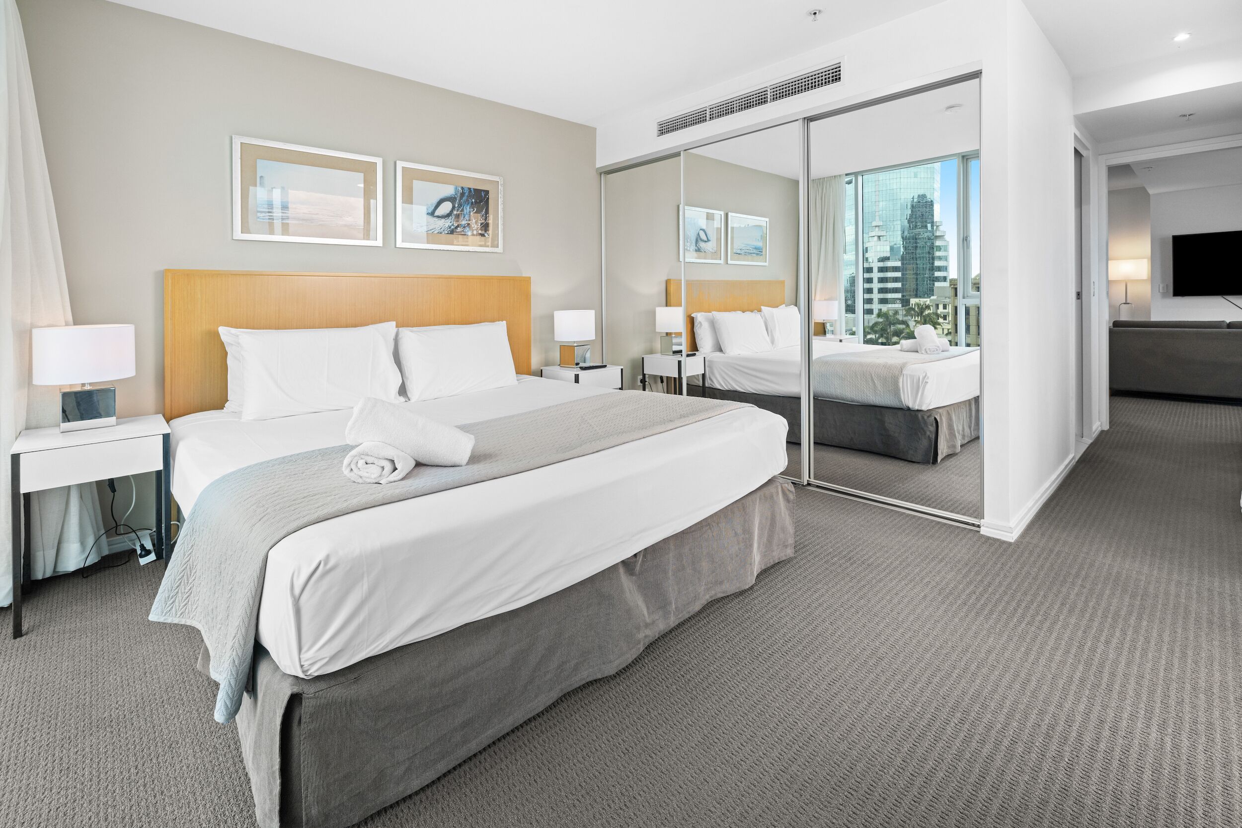 Une chambre d’hôtel moderne dotée d’un grand lit, d’un bureau, d’un téléviseur à écran plat et offrant une vue sur la ville grâce à la porte vitrée.
