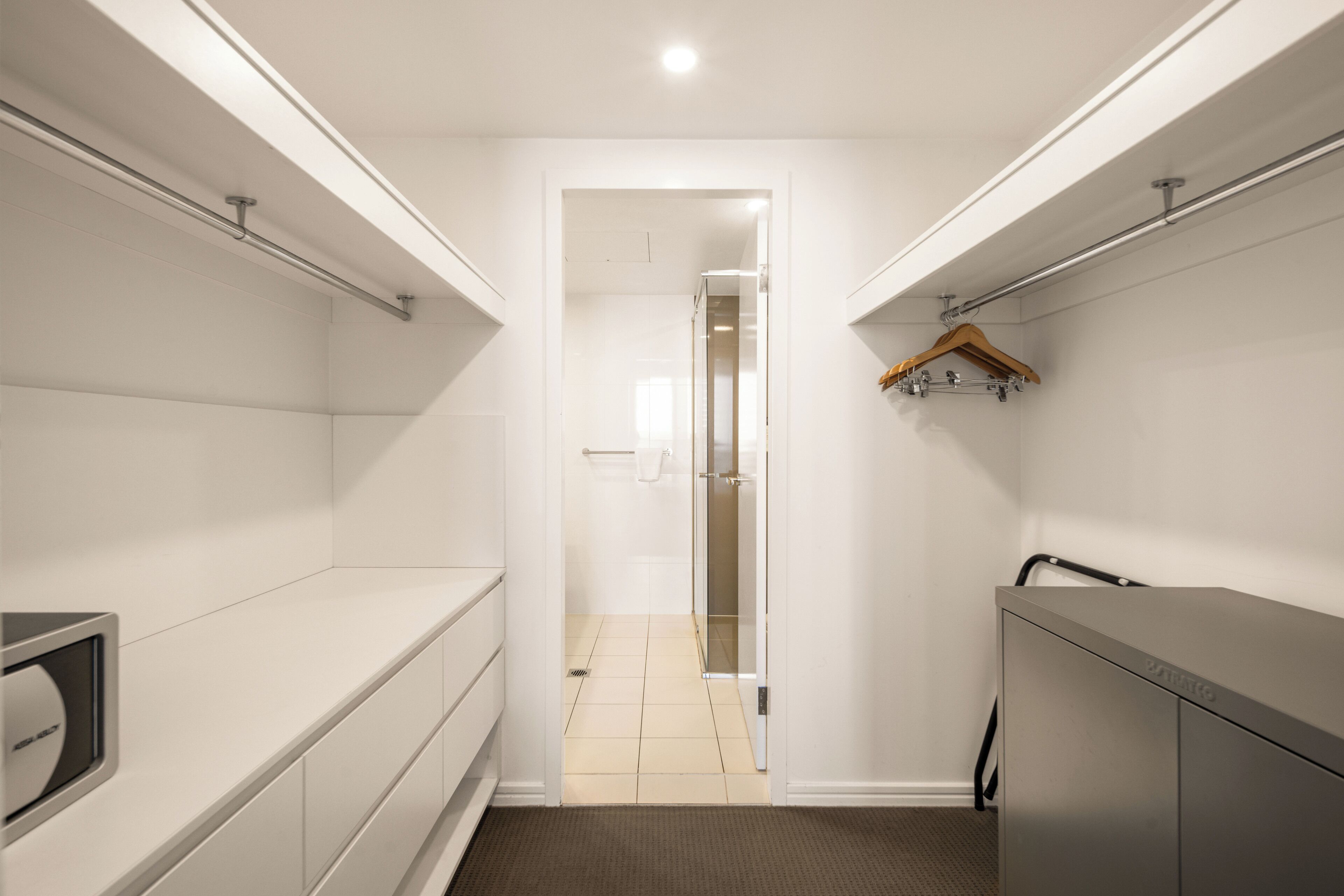 Un couloir étroit avec un miroir, un porte-manteau et une porte donnant sur une autre pièce.