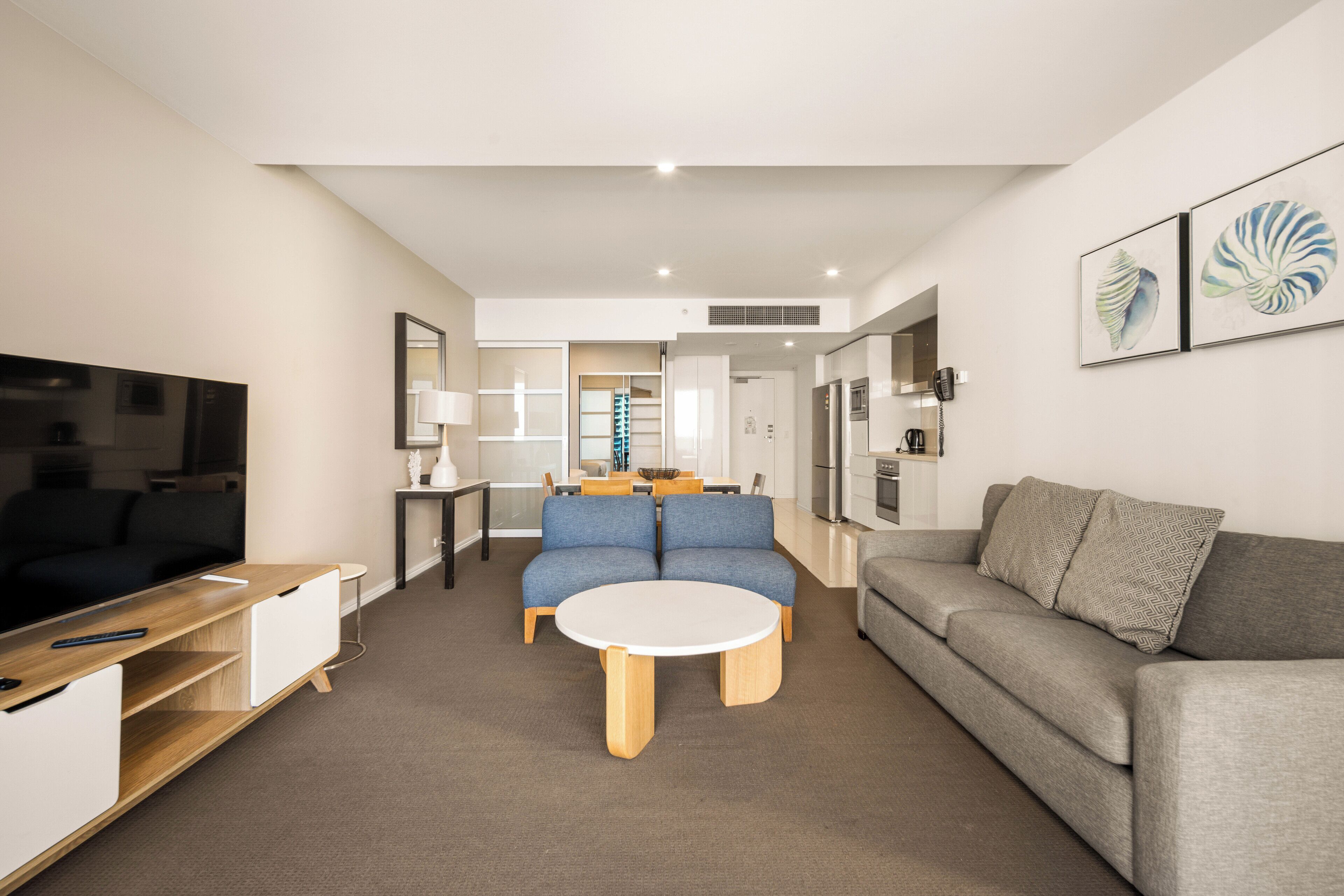 A modern living room with a flat-screen TV, a grey sofa, a blue sofa, and a round coffee table.