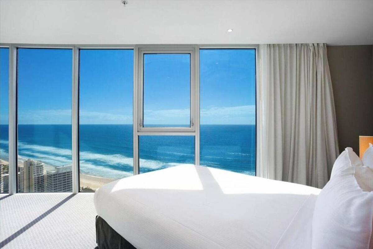Habitación de hotel con una cama grande, vista al océano y al paisaje urbano.