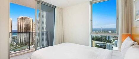 A hotel room with a large bed, a sliding glass door to a balcony, and a view of city buildings.