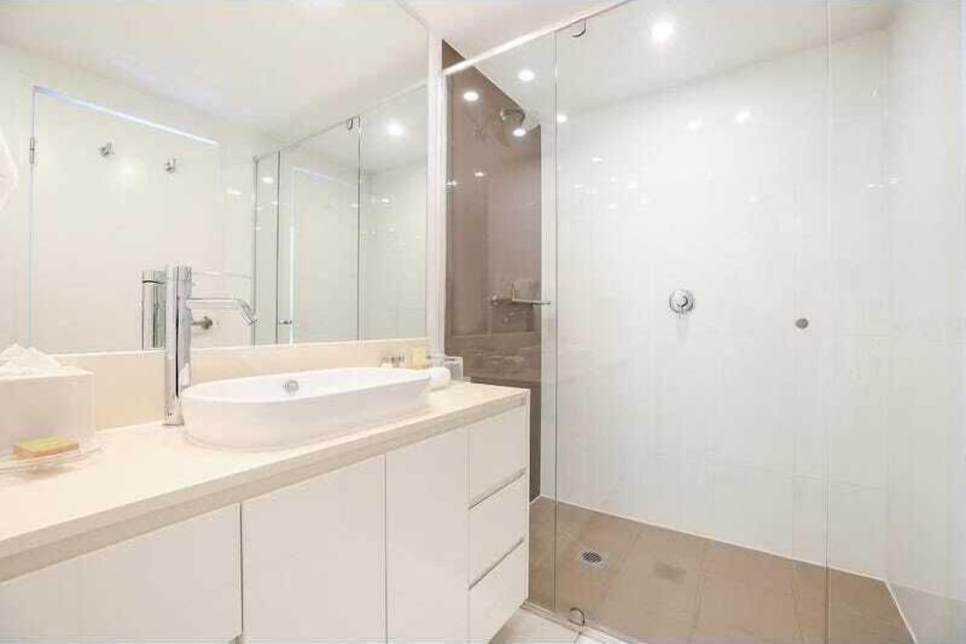 Une salle de bain moderne avec un grand miroir, un lavabo blanc et une douche séparée par des parois en verre.