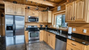 Una cocina moderna con armarios de madera, electrodomésticos de acero inoxidable, encimeras de granito y un amplio ventanal.