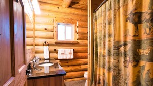 Un baño de cabaña de troncos con interior de madera, un lavabo, una ventana y una cortina de ducha con motivos naturales.