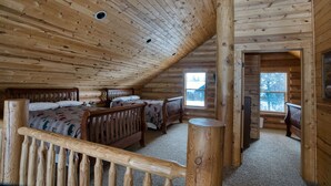 Un dormitorio de cabaña de madera con dos camas, techo de madera y ventana con vistas al exterior.