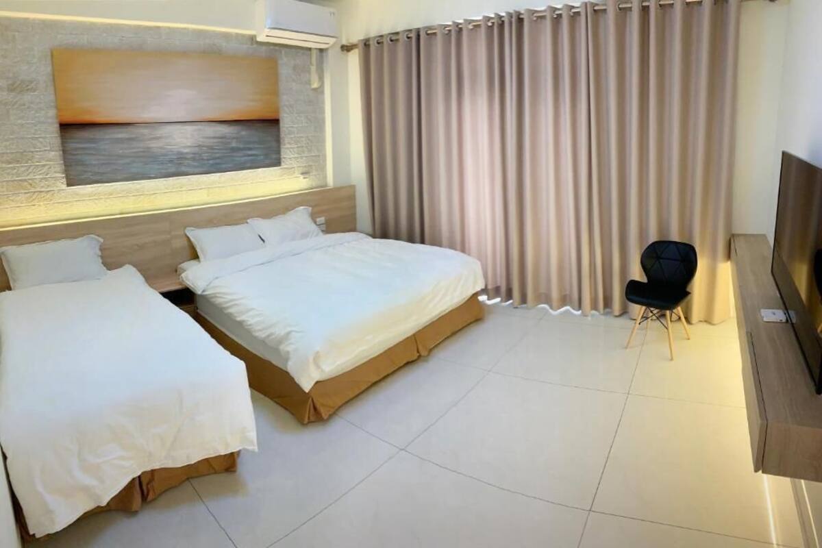 A hotel room with a large bed, a smaller bed, a TV, a chair, and a painting on the wall.