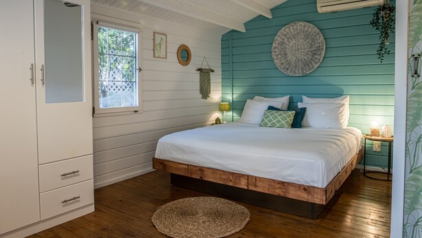 Un dormitorio con una cama de madera, paredes blancas, una ventana y un armario blanco.