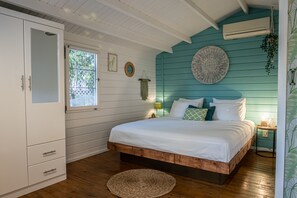Une chambre à coucher avec un lit en bois, des murs blancs, une fenêtre et une armoire blanche.