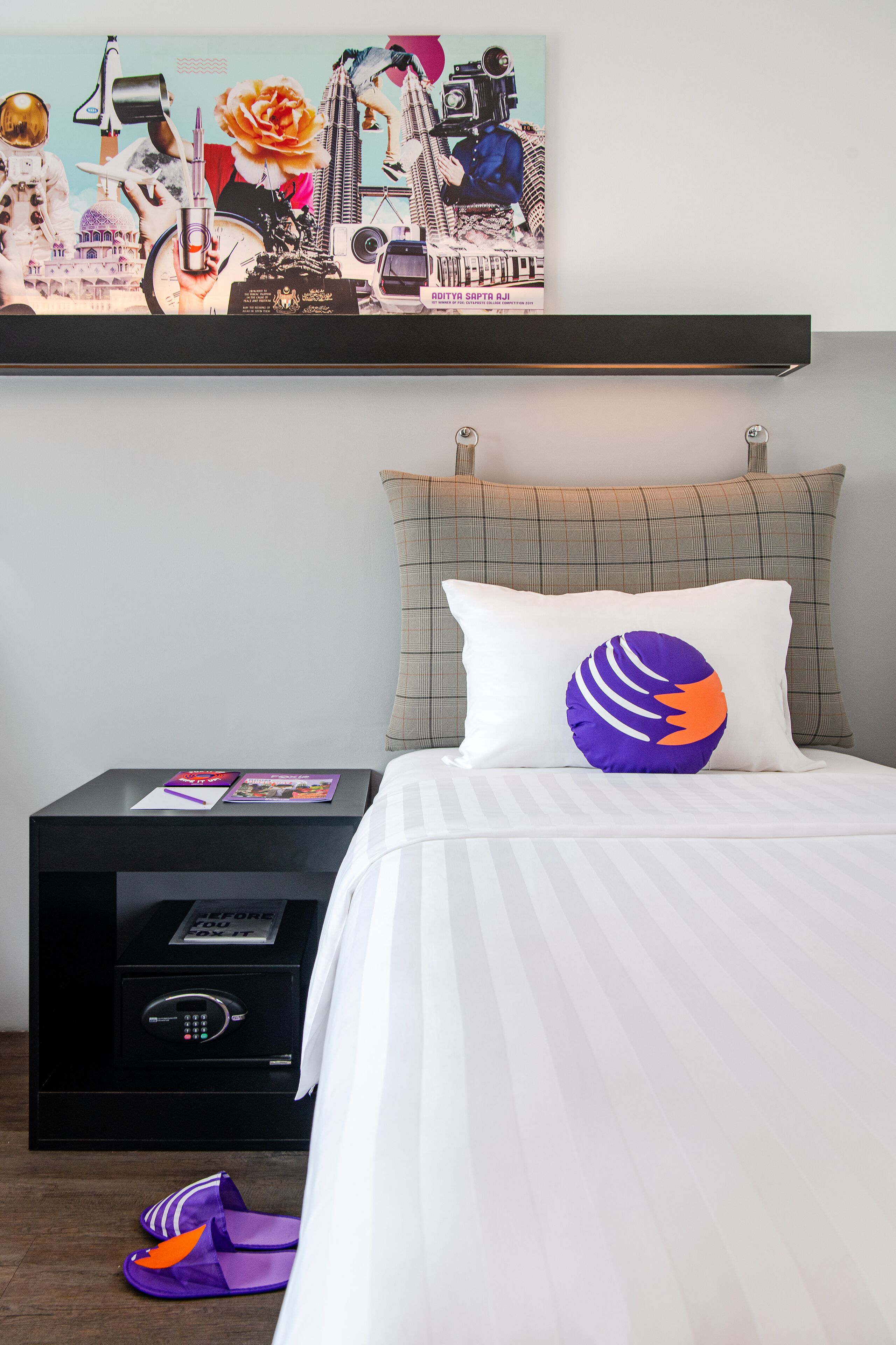 Ein Hotelzimmer mit einem Bett, einem Nachttisch, einem an der Wand hängenden Kunstwerk und einem Paar Hausschuhen auf dem Boden.
