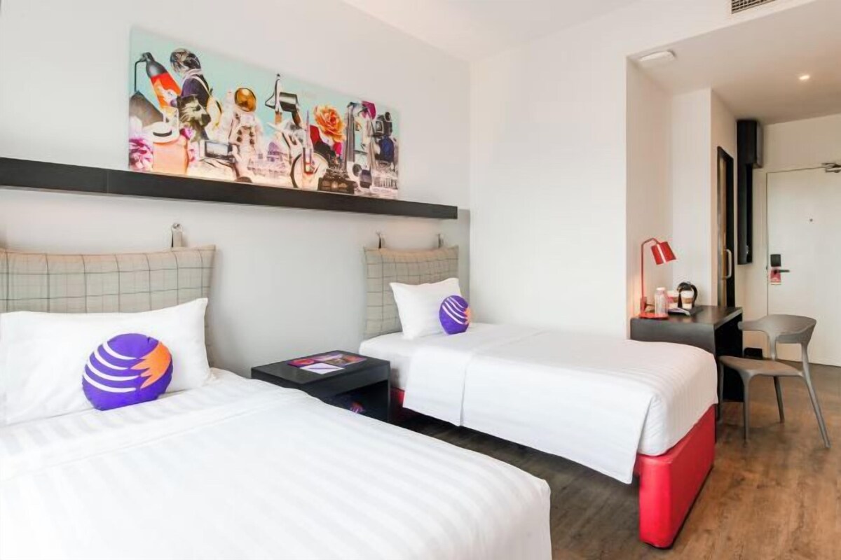 Une chambre d’hôtel avec deux lits, un bureau, une chaise et un grand tableau abstrait accroché au mur.