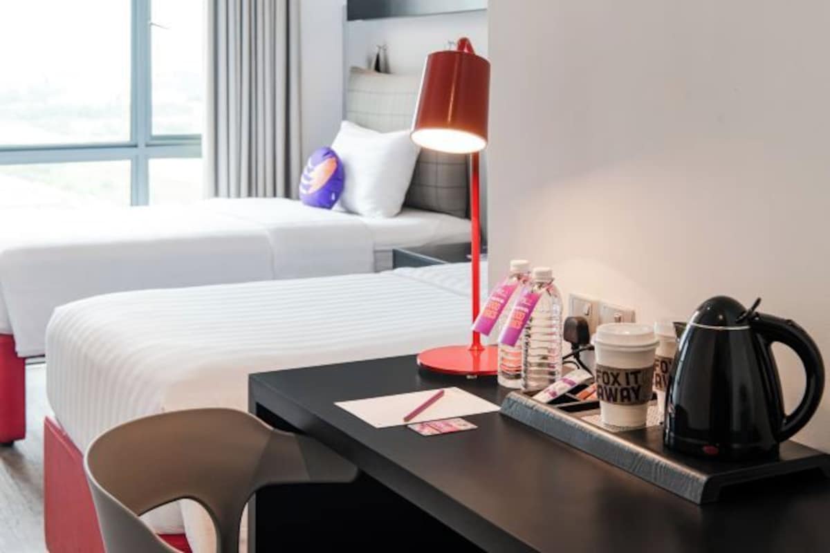 Habitación de hotel con dos camas, un escritorio con lámpara, cafetera y una bandeja con botellas y una taza.