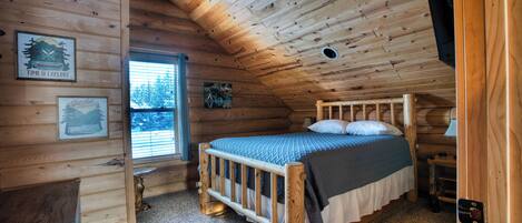 A cozy cabin room with a wooden bed, a window with blinds, and a door.