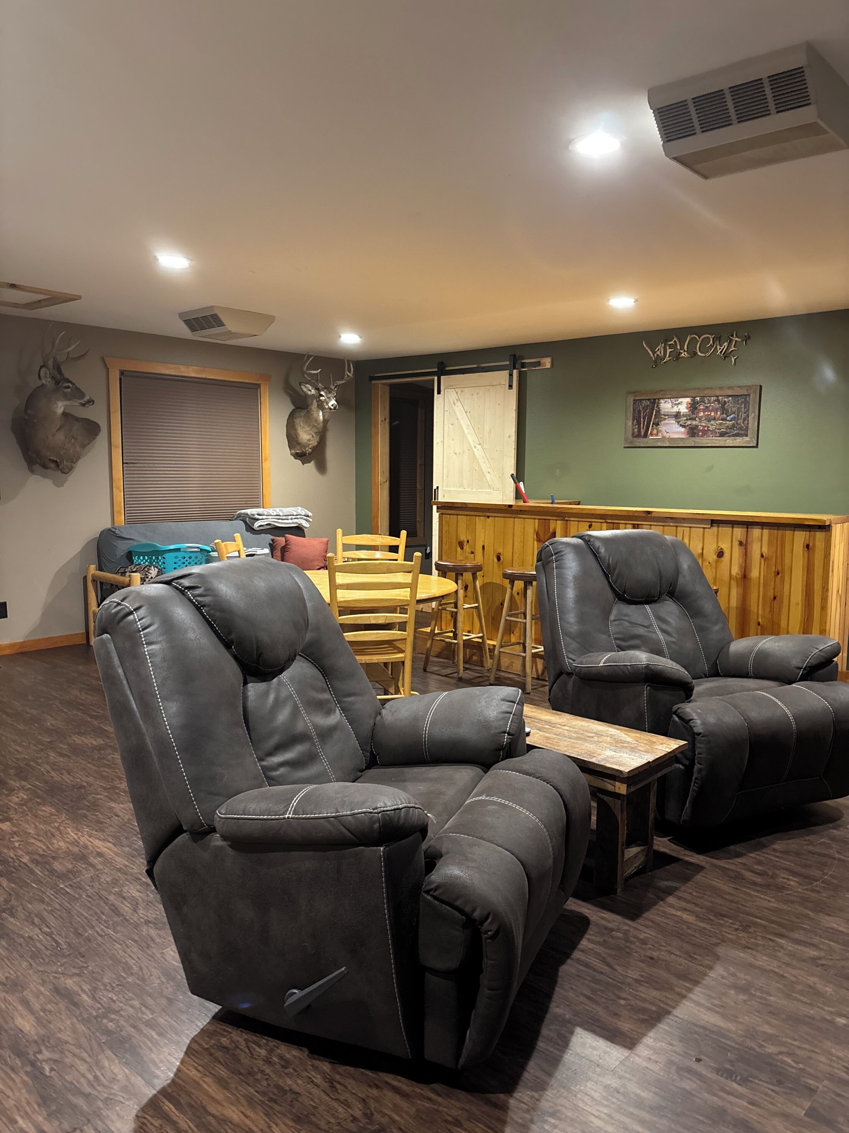 Een kamer met twee ligstoelen, een houten tafel, een bank en een aan de muur bevestigd hertenhoofd.