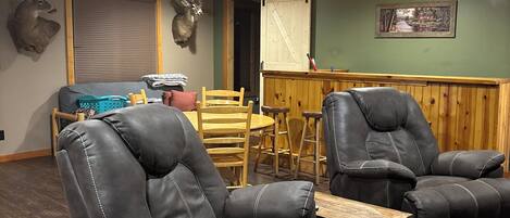 A room with two reclining chairs, a wooden table, a bench, and a wall-mounted deer head.