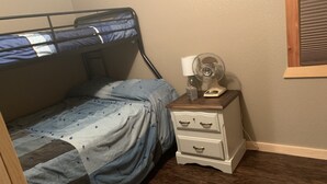 Una cama individual en literas con una colcha de diseño azul y blanco, una mesita de noche con cajones, una lámpara y un ventilador.