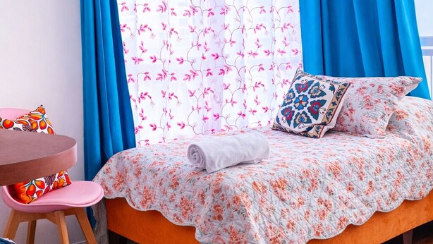 Ein Schlafzimmer mit einem Bett, einem Sessel, einem kleinen Tisch und einem Fenster mit Vorhängen.