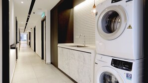 A hotel laundry room with a washing machine and dryer, a sink, and a tiled wall. - Z Hotel (Petaling Jaya)
