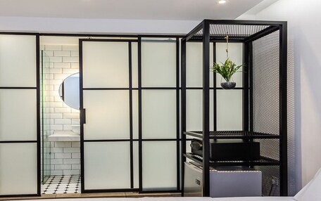A modern bedroom with a grey upholstered headboard, a black storage unit, and a sliding glass door with frosted panels.