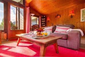 Une pièce chaleureuse avec un plafond en bois, un canapé agrémenté de coussins à rayures, une table où sont disposés des éléments pour le petit-déjeuner et une bibliothèque.