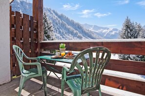 Een houten terras met een tafel en stoelen, met uitzicht op een besneeerd berglandschap.