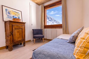 Une chambre à coucher avec un lit, une chaise, une armoire en bois, une fenêtre donnant sur des montagnes enneigées et un tableau accroché au mur.