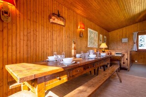 Een houten interieur met een lange eettafel gedekt voor een maaltijd, houten wanden en een raam met uitzicht.