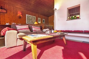 Un salon chaleureux avec un plafond en bois, un canapé agrémenté de coussins à rayures, une table basse et un coin repas avec un banc.