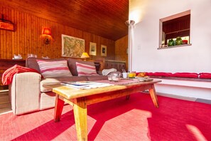 Un salon chaleureux avec un plafond en bois, un canapé agrémenté de coussins à rayures, une table basse et un tapis rouge.
