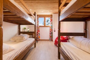 Een kamer met twee stapelbedden, een klein tafeltje met een lamp en een raam met gordijnen.