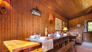 Een houten interieur met een lange eettafel gedekt voor een maaltijd, houten wanden en een raam met gordijnen.
