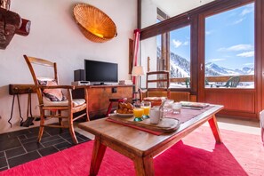 Een gezellige kamer met een houten ontbijttafel, een televisie en uitzicht op besneeuwde bergen.