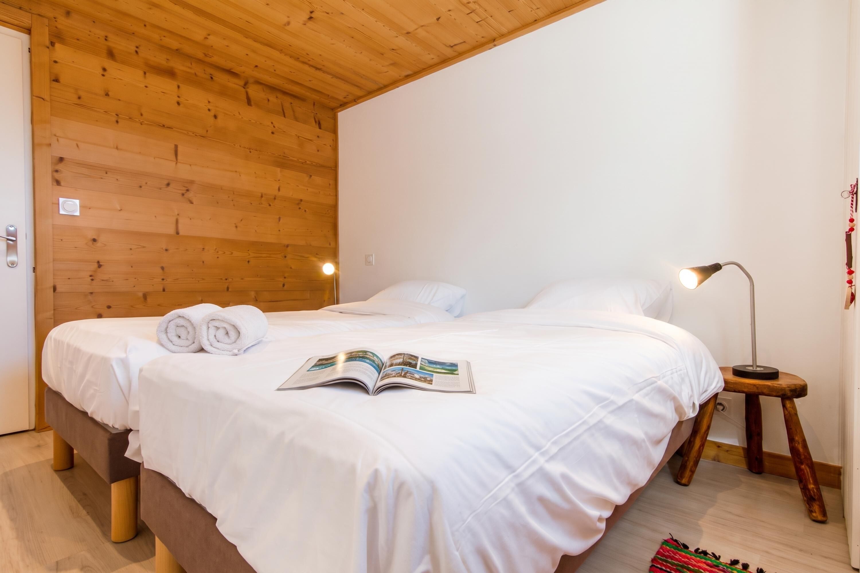Una cama bien tendida con sábanas y toallas blancas, una lámpara de noche y un libro sobre la cama.