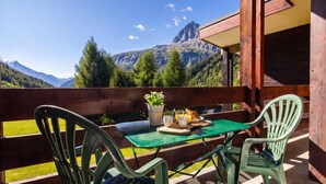 Een balkon met een tafel en stoelen, uitkijkend op een bergachtig landschap.