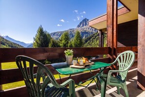 A balcony with a table and chairs, overlooking a mountainous landscape.