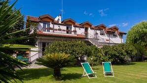 A multi-story building with a tiled roof, balconies, and a well-maintained lawn with two green lawn chairs.