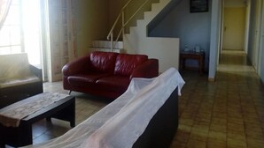 A living room with a red sofa, a small table, and a staircase leading to another level. - Gîte Océania (Wallis Island)