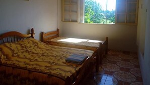 A room with two wooden beds, a window with a view of greenery, and a ceiling fan. - Gîte Océania (Wallis Island)
