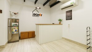 A reception area with a wooden counter, a refrigerator with Sanyo branding, a potted plant, and a wall-mounted sign. - The Eighty8 Hanoi Hostel (Hanoi)
