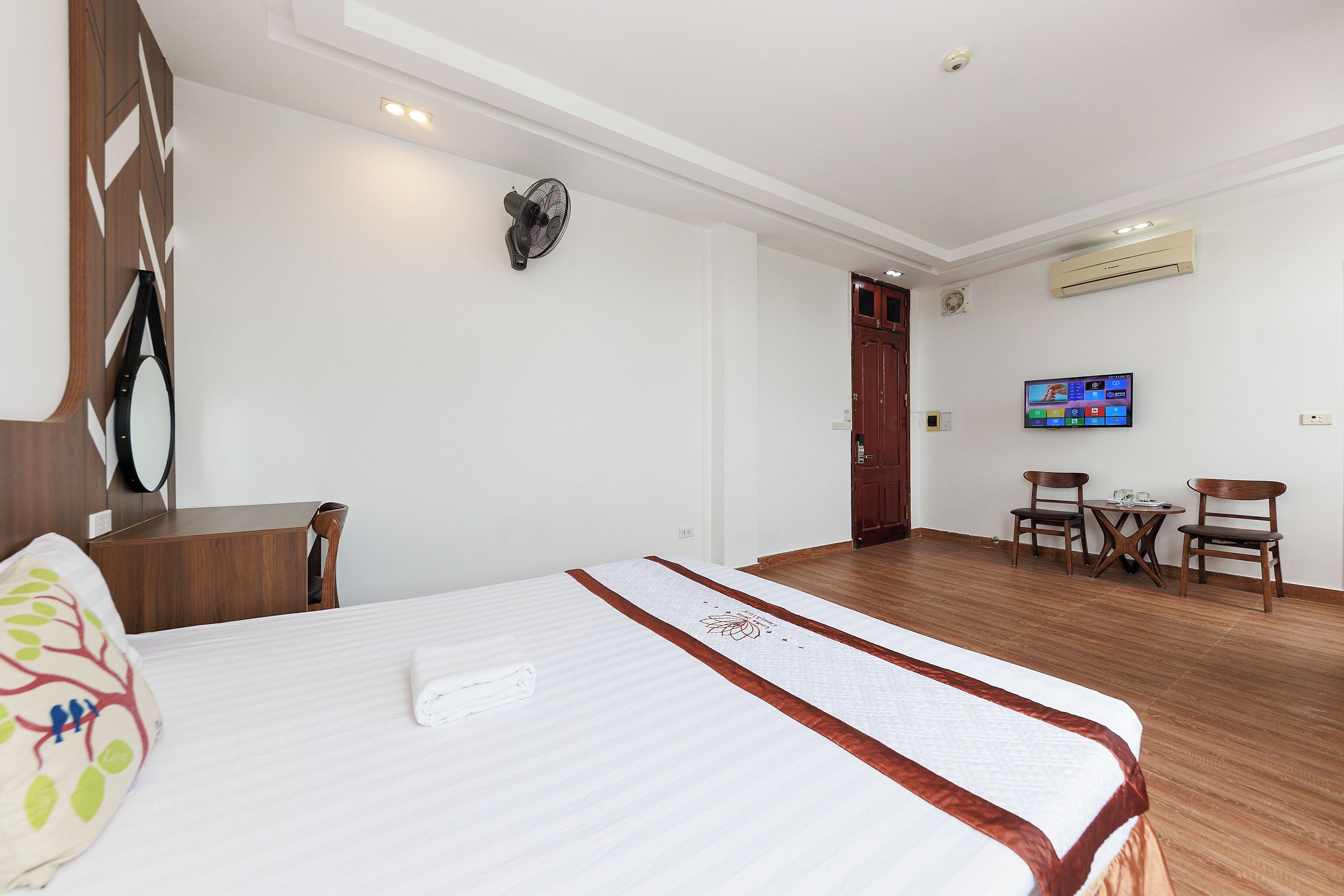 A hotel room with a bed, a desk, a chair, a TV, and an air conditioning unit.