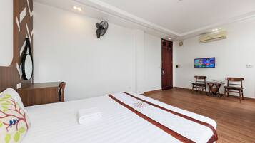 A hotel room with a bed, a desk, a chair, a TV, and an air conditioning unit.