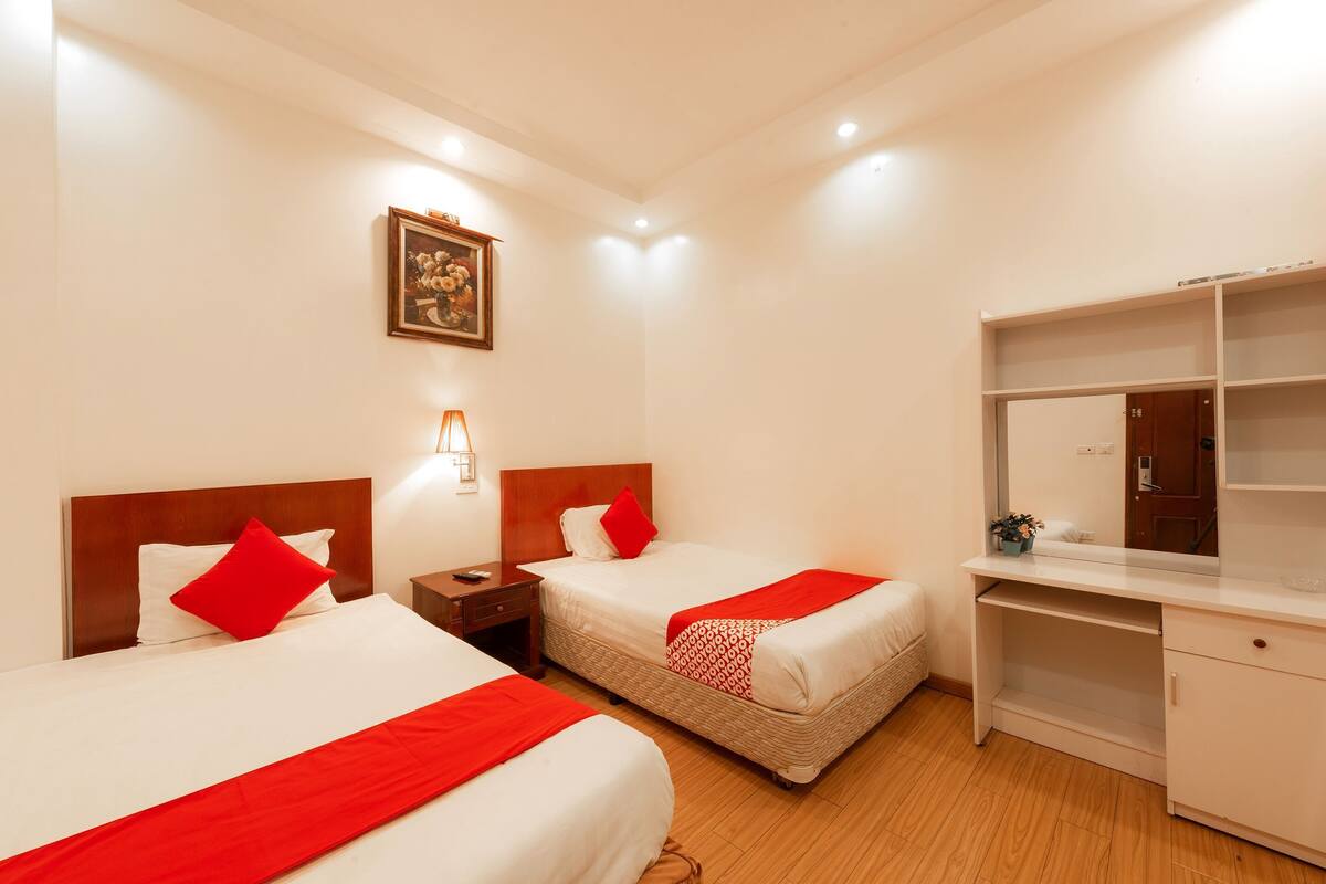 A hotel room with two beds, a desk, a wardrobe, and a framed picture on the wall.