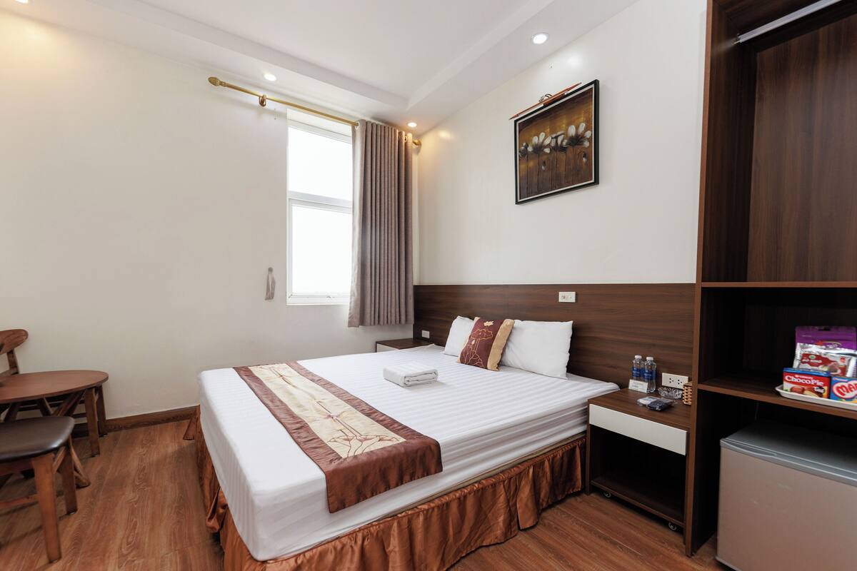 A hotel room with a large bed, a desk, a chair, a wardrobe, and a window with curtains.